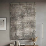 This rug features an understated abstract design in cream and grey tones, finished with a defined geometric border along the edges. The pile is intentionally low and soft, giving it a smooth, premium feel underfoot. It delivers a clean, high-quality look using simple, neutral colors.