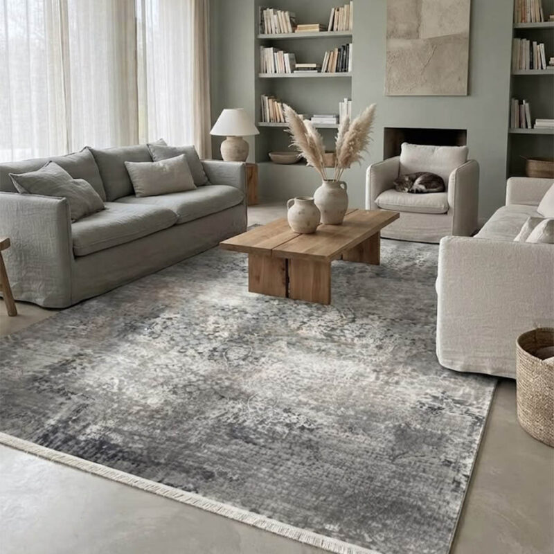 This rug features an understated abstract design in cream and grey tones, finished with a defined geometric border along the edges. The pile is intentionally low and soft, giving it a smooth, premium feel underfoot. It delivers a clean, high-quality look using simple, neutral colors.