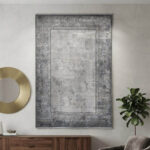 A high-quality area rug with a soft, uniform surface that feels smooth to the touch. The design showcases a distressed, abstract blend of grey and off-white in the center, bordered by a sharp, geometric frame. It offers a premium look and a comfortable feel without unnecessary embellishments.