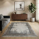 Modern abstract area rug in grey and beige tones styled in a minimalist living room with a grey sofa and wooden credenza.