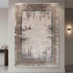 Modern abstract area rug in grey and beige tones styled in a minimalist living room with a grey sofa and wooden credenza.
